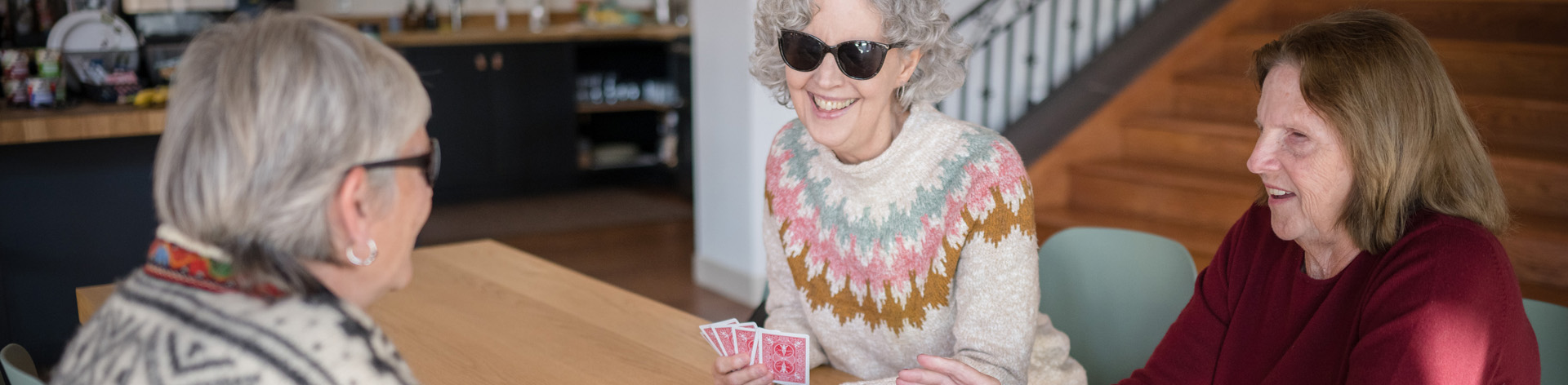 Three senior women smile and play cards together.